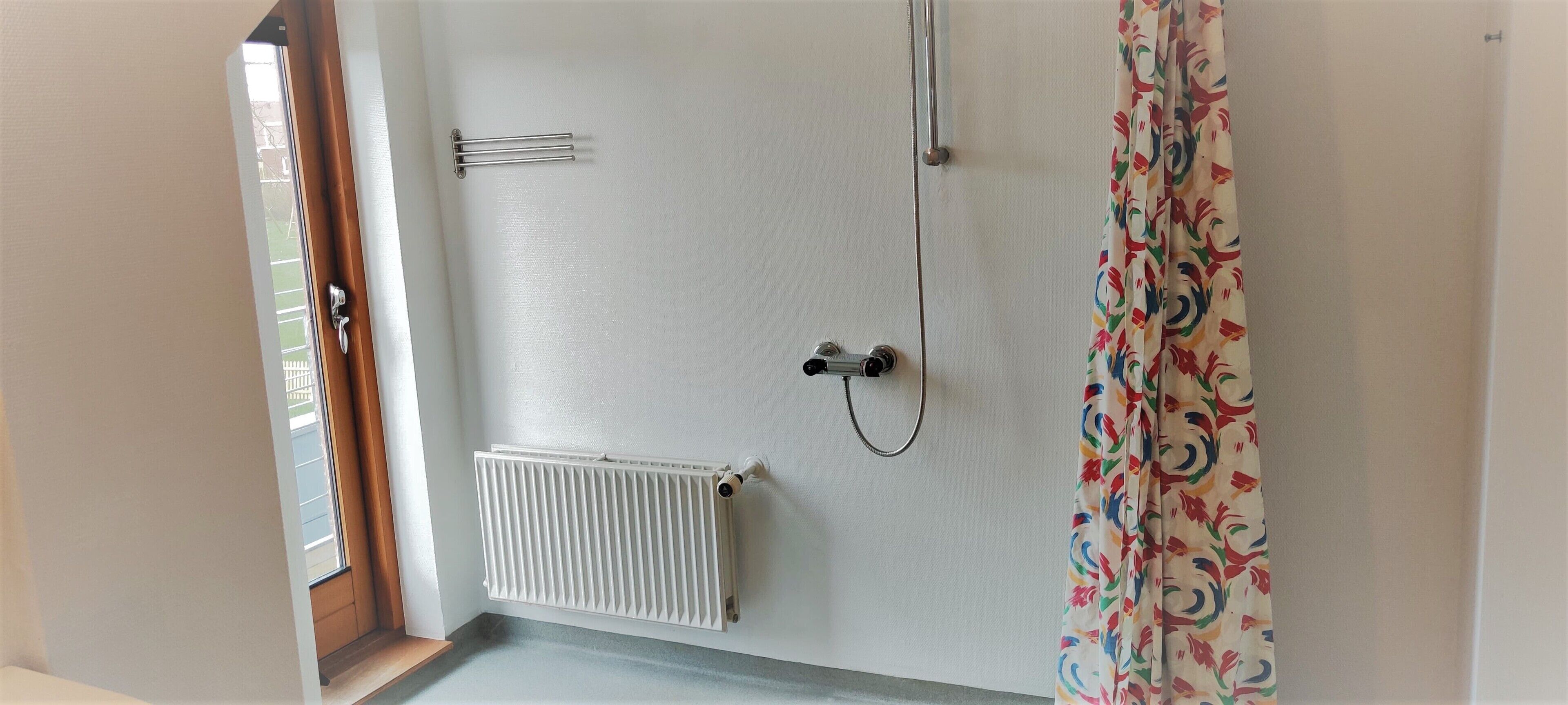Et badeværelse med en hvid radiator, en bruser og et farverigt gardin.