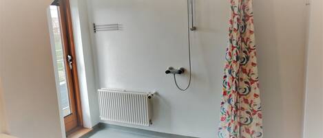 Et badeværelse med en hvid radiator, en bruser og et farverigt gardin.