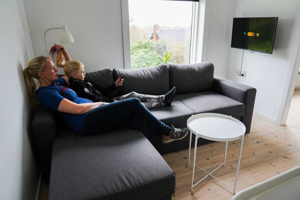 A modern living room with a grey sofa, a small white table, and a TV mounted on the wall.
