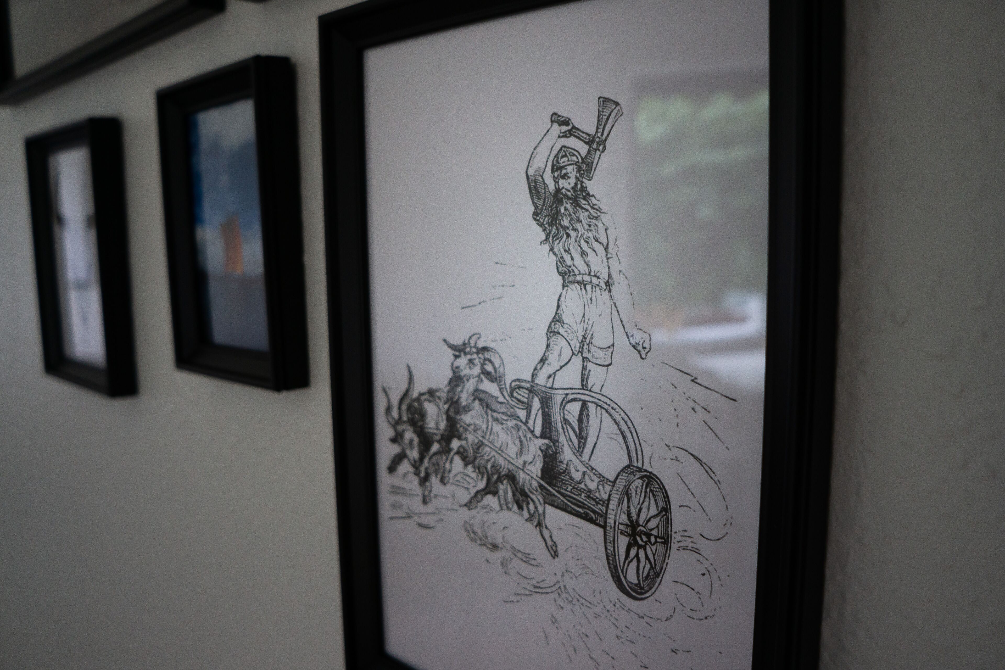 Una ilustración en blanco y negro enmarco muestra a una persona montando en un carruaje tirado por caballos.