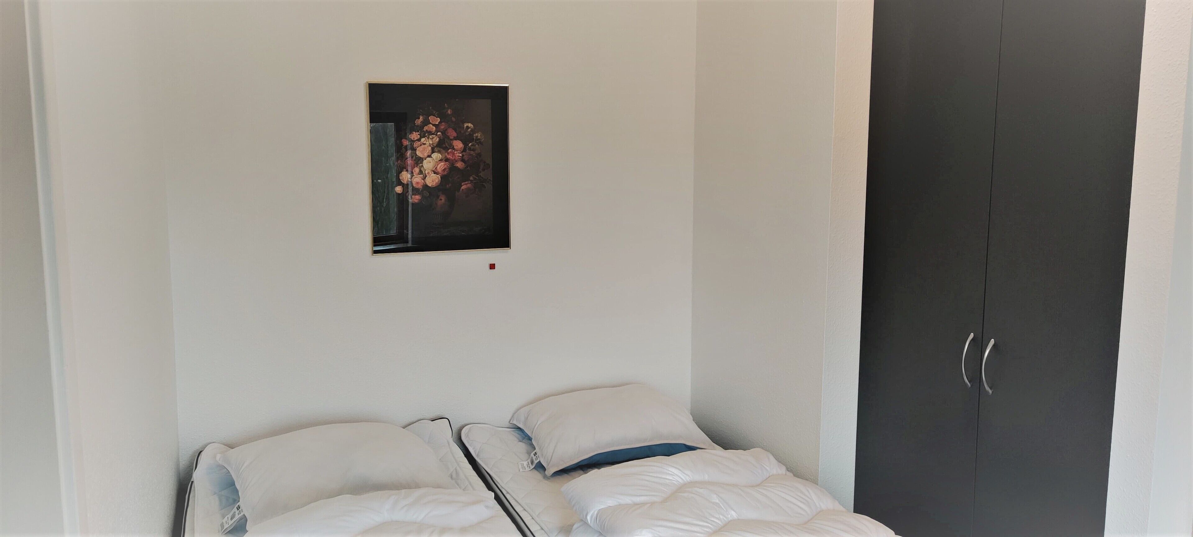 A bedroom with a bed, a dark wardrobe, and a framed picture on the wall.