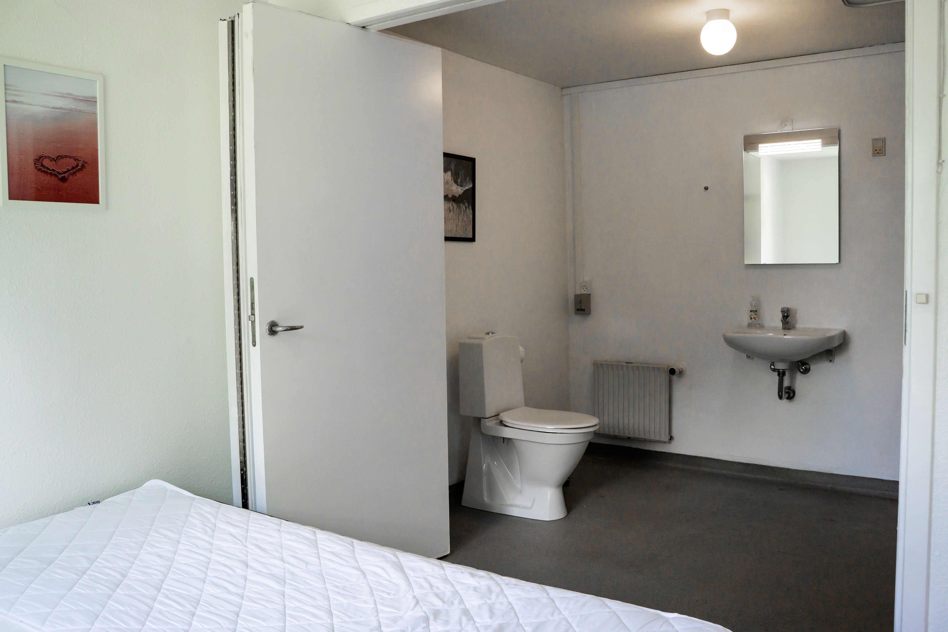 Ein Schlafzimmer mit Bett, ein Badezimmer mit Toilette, Waschbecken und Spiegel.