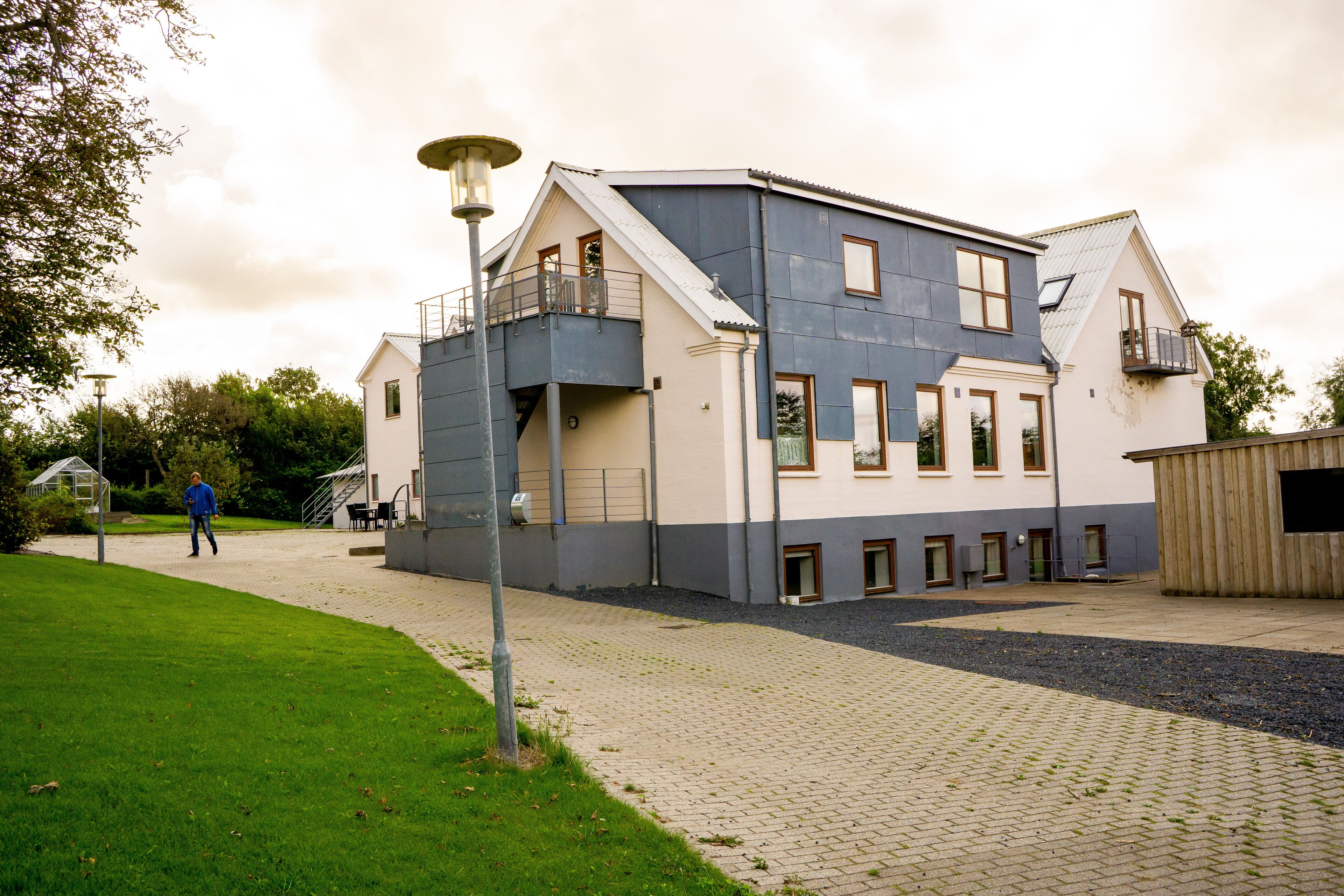 Une maison moderne à deux étages, dotée d’un balcon, d’un espace extérieur couvert et d’une allée pavée.