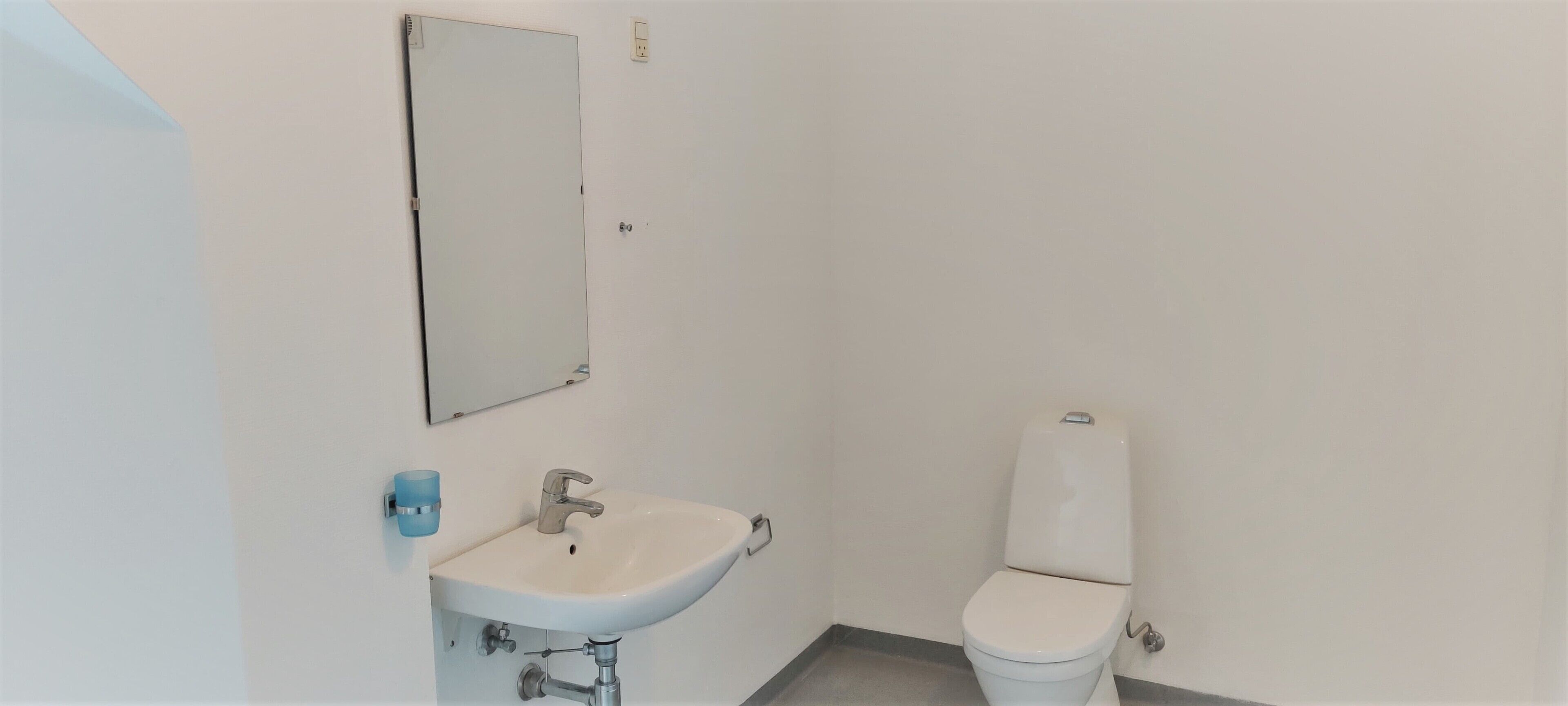 A small, clean bathroom with a white sink, mirror, and toilet.
