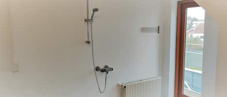 Un baño con ducha, radiador y ventana con vistas a edificios.