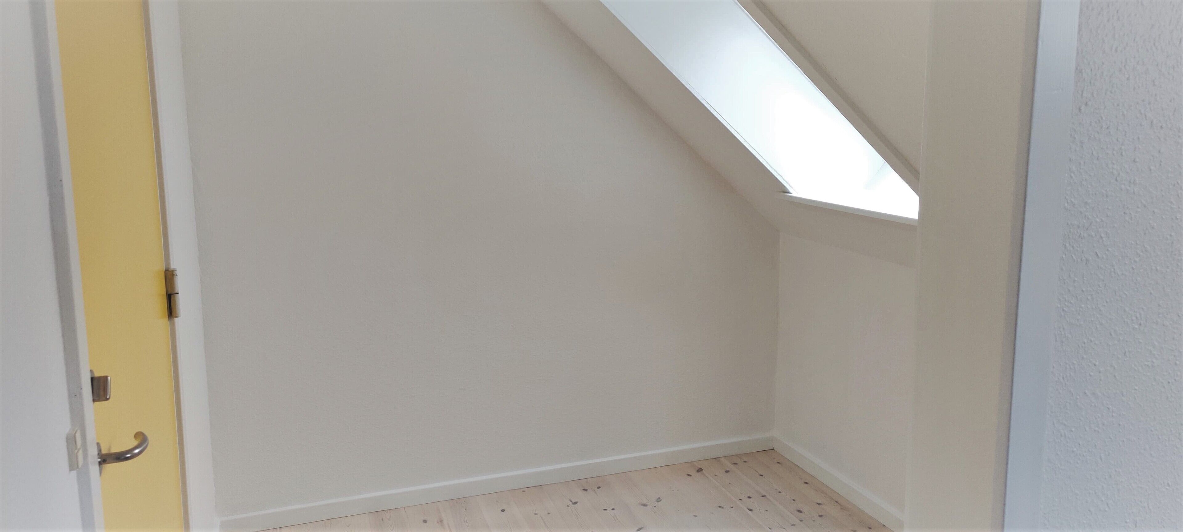 Una habitación con techo inclinado, tragaluz y suelo de madera.