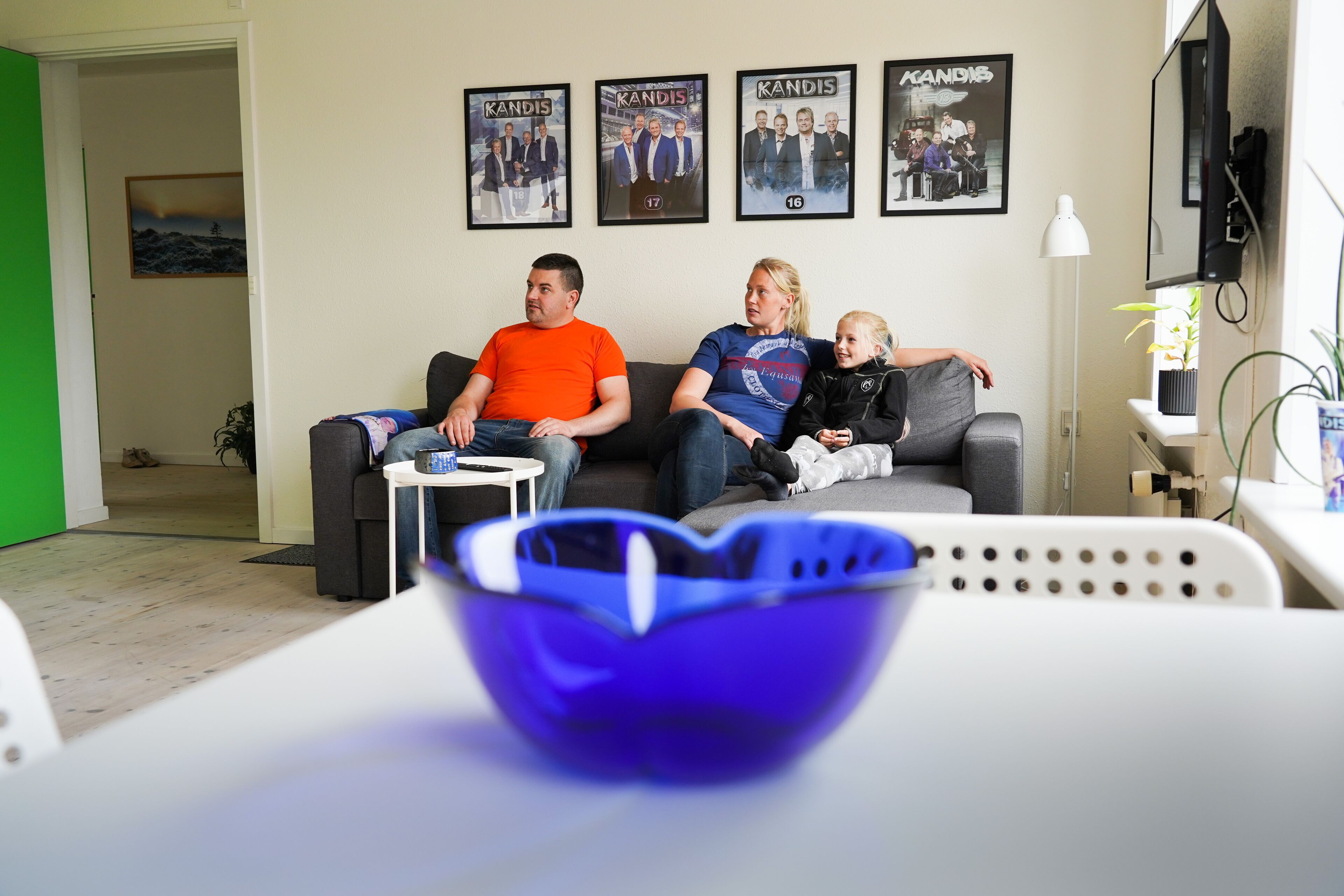 Un salon avec un canapé, une table basse sur laquelle se trouve un bol bleu, et des affiches encadrées accrochées au mur.