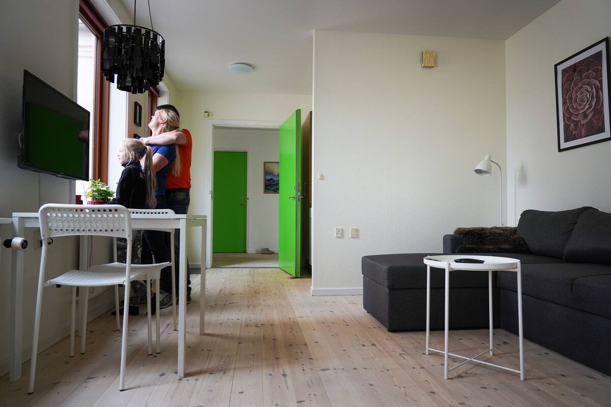 A modern living room with a flat-screen TV, a dining table with chairs, a black sofa, and a small white side table.