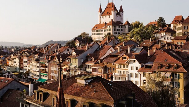 A historic castle with a prominent tower, surrounded by traditional European buildings with red-tiled roofs. - Boutique Hotel Schlossberg (Thun)