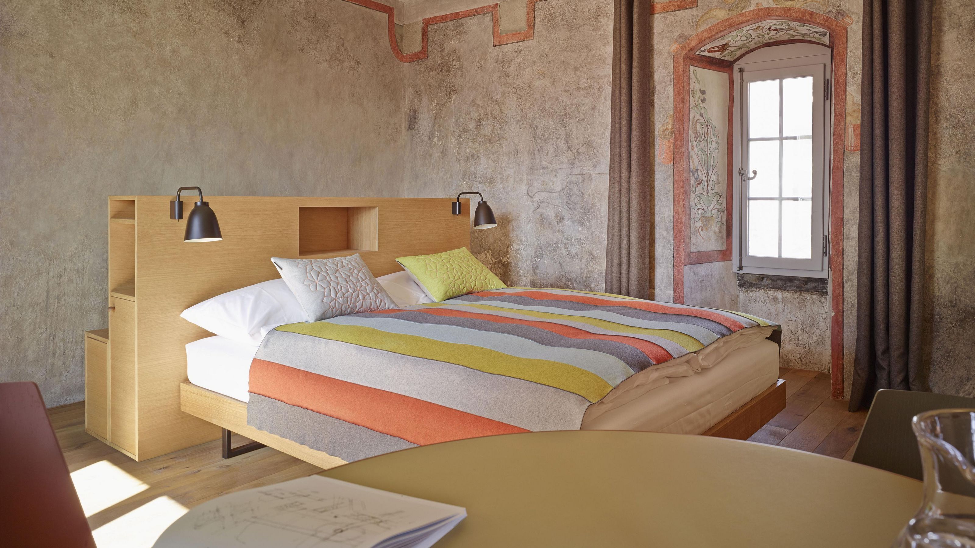A modern bedroom with a wooden headboard, a striped bedspread, and a nightstand with a lamp.