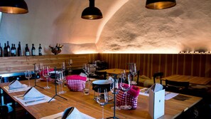 Un restaurante con mesas de madera, copas de vino y botellas en la pared.
