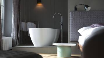 Un baño moderno con una bañera independiente, un lavamanos adosado a la pared y una mesita de noche.