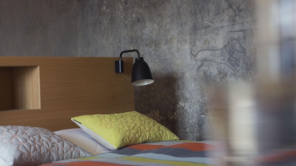 Una cama con un colcha colorida, un cabecero de madera y una lámpara de escritorio negra.