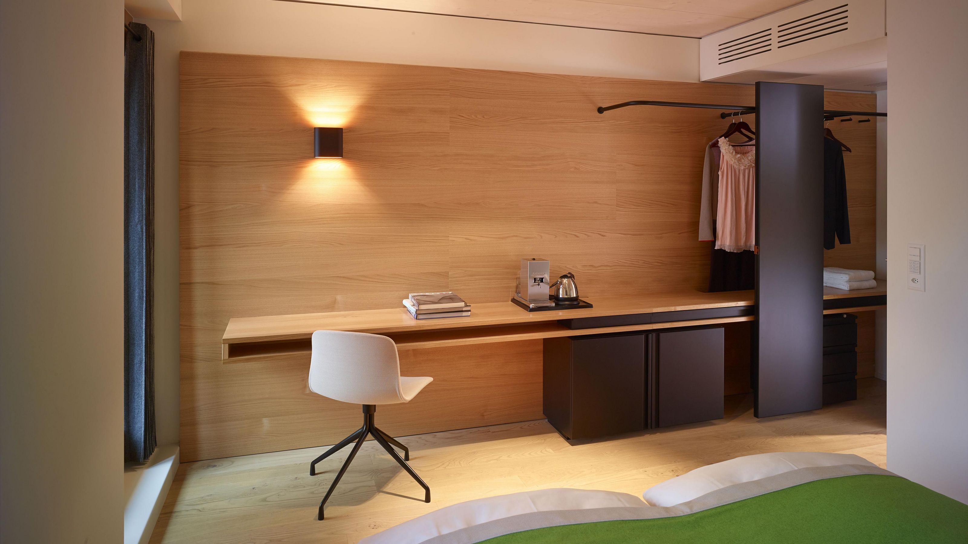 Ein modernes Schlafzimmer mit Holzwand, Schreibtisch, Stuhl und einer hängenden Garderobe.