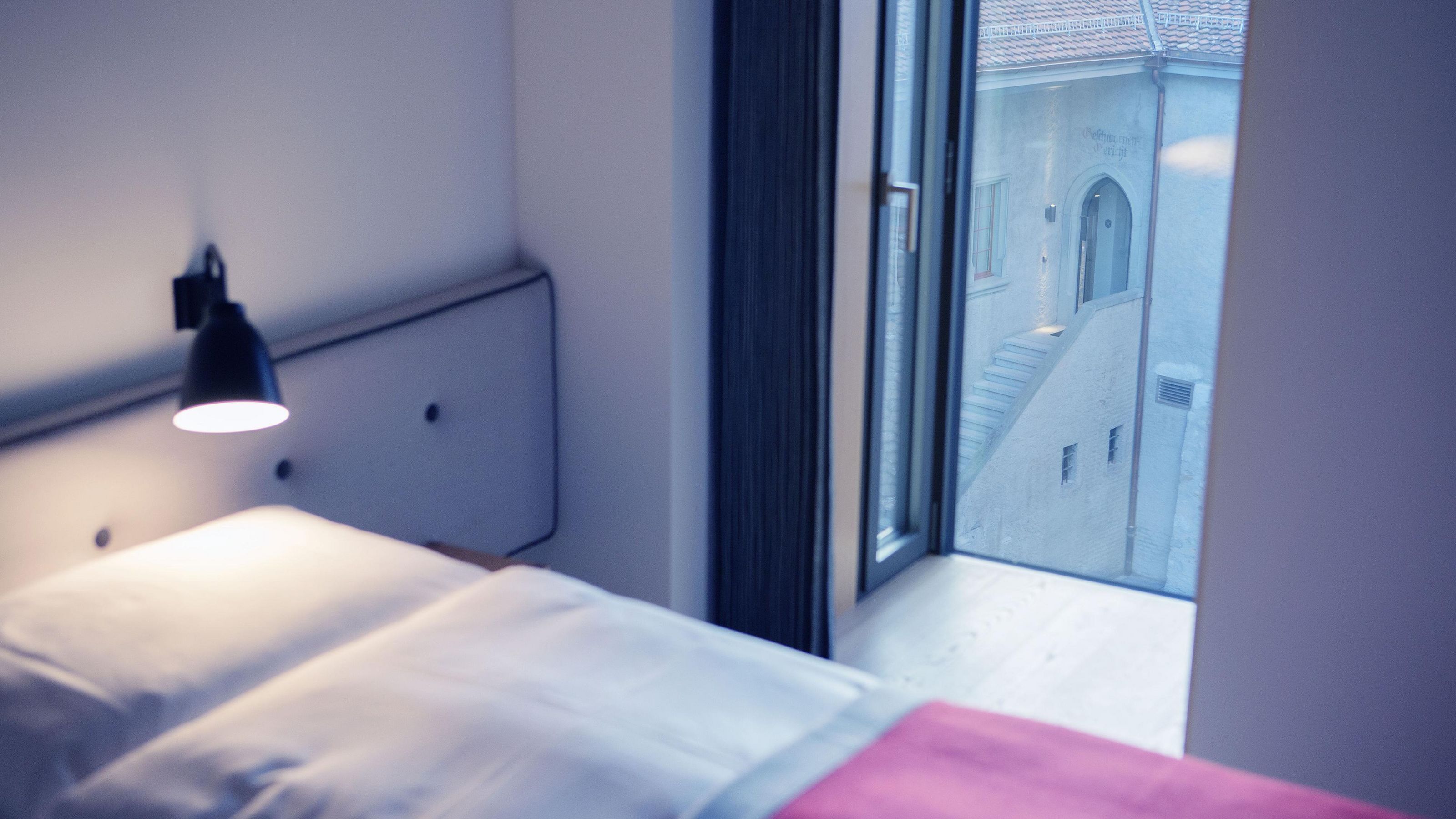Una camera da letto con un letto, una lampada da comodino e una finestra che dà su un edificio con una scala.