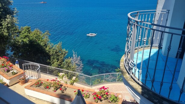 A balcony with a view of the sea, a boat, and a flower bed. - L'Incanto Suites Ischia (Casamicciola Terme)
