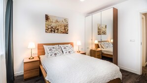 Un dormitorio ordenado con una cama grande, dos mesitas de noche con lámparas, un espejo y una obra de arte floral en la pared.