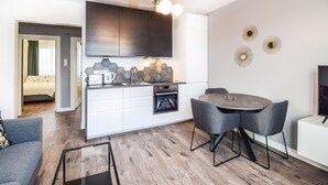 Una cocina moderna con horno integrado, un comedor con mesa redonda y sillas, y un televisor de pantalla plana grande sobre un mueble blanco.
