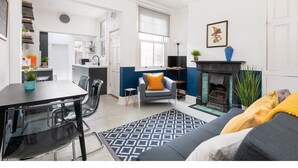 A modern living room with a fireplace, a dining area with a table and chairs, and a kitchen in the background. - Charming & Trendy Base for 5, nr Bishopthorpe Rd (York)