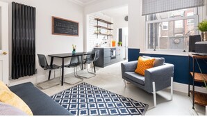 A modern kitchen with a chalkboard menu, a dining area with a black table and chairs, a blue patterned rug, and a grey sofa with an orange pillow. - Charming & Trendy Base for 5, nr Bishopthorpe Rd (York)