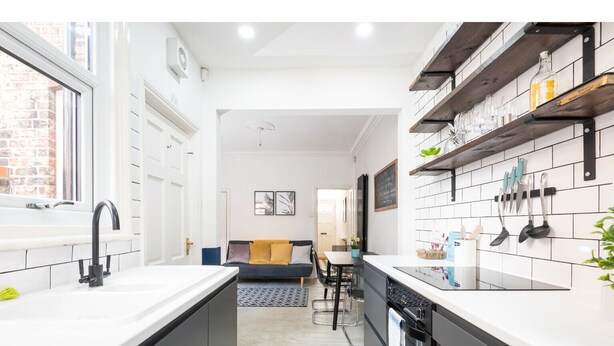 A modern kitchen with white countertops, black cabinets, and a dining area with a sofa and table. - Charming & Trendy Base for 5, nr Bishopthorpe Rd (York)