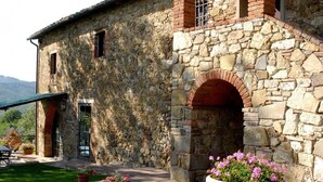 Un bâtiment en pierre à l’aspect rustique, doté d’une grande porte d’entrée en arc de cercle et d’un petit balcon agrémenté d’une table et de chaises.