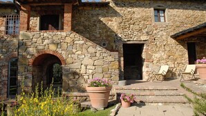 Un bâtiment en pierre avec une arche en briques, une petite fenêtre et une porte. Des marches mènent à un porche doté de sièges extérieurs.