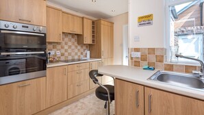 A modern kitchen with wooden cabinets, a built-in oven, and a window with a view of the outside. - Cosy Home 5 Minute Walk to Monkbar and Bar Walls! (York)