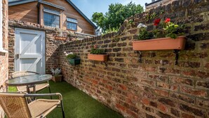 A brick wall with hanging planters, a white door, and a small table with chairs. - Cosy Home 5 Minute Walk to Monkbar and Bar Walls! (York)