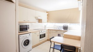 A compact kitchen with a washing machine, microwave, oven, and a small dining area with two chairs. - 2BD Apartment, 500m From Windsor Castle, Parking (Windsor)