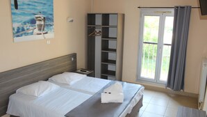 A hotel room with two beds, a wardrobe, a bathroom, and a window with curtains. - Les Voiles d'Azur (La Londe-les-Maures)