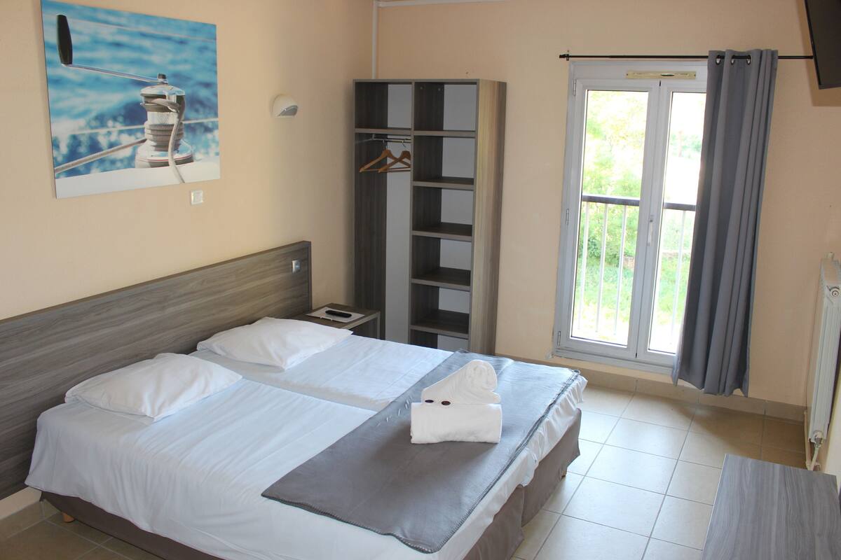 Habitación de hotel con dos camas, un armario, un baño y una ventana con cortinas.