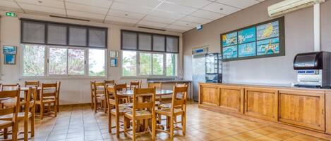 Un restaurant avec des tables et des chaises en bois, de grandes fenêtres et un sol carrelé.