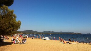 A beach with people sunbathing and swimming, boats in the water, and a clear sky. - Les Voiles d'Azur (La Londe-les-Maures)