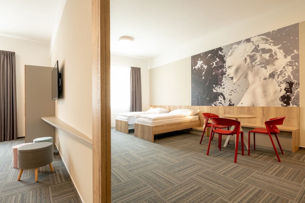 A modern hotel room with a bed, a desk, and a large abstract painting on the wall.