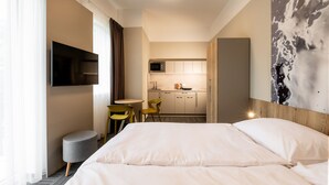 Une chambre d’hôtel comprenant un lit, un téléviseur fixé au mur, une petite kitchenette et un coin repas avec des chaises.