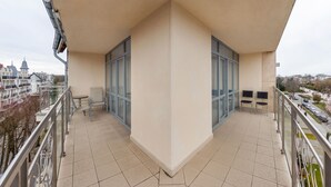 A balcony with a tiled floor, two chairs, a small table, and a glass door leading to an indoor area.