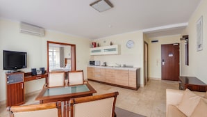 A living room with a TV, wooden furniture, a dining table, and a kitchen area with cabinets and appliances.