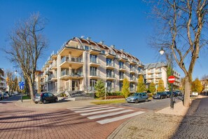 Un immeuble résidentiel à plusieurs étages, doté de balcons, d’un passage piéton et de voitures garées.