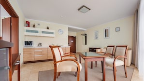 A modern kitchen with wooden cabinets, a microwave, and a coffee maker. There is a dining area with a glass-top table and wooden chairs.