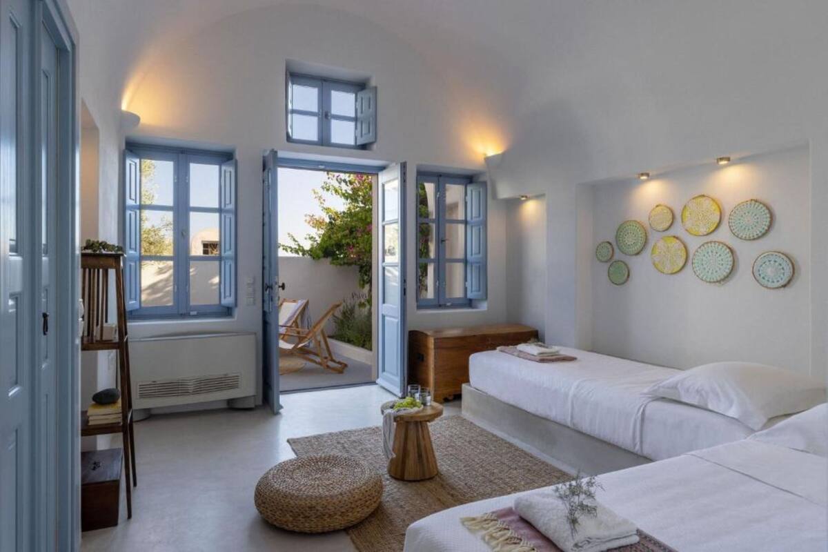 A room with two beds, a wooden chest of drawers, a small round table with a plant, and a wall with circular decorative plates.