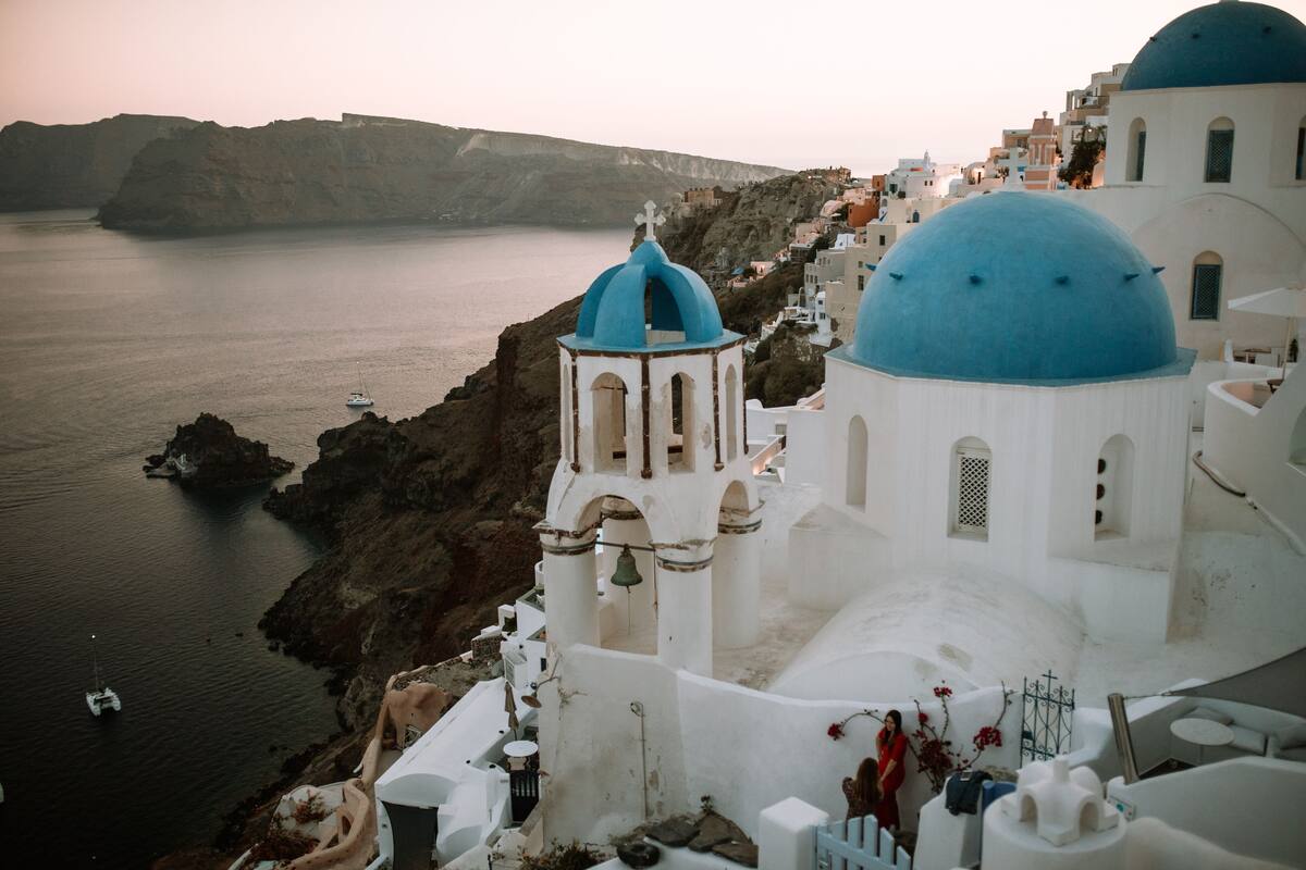 A coastal building with white and blue domed architecture, overlooking a body of water and rocky cliffs.