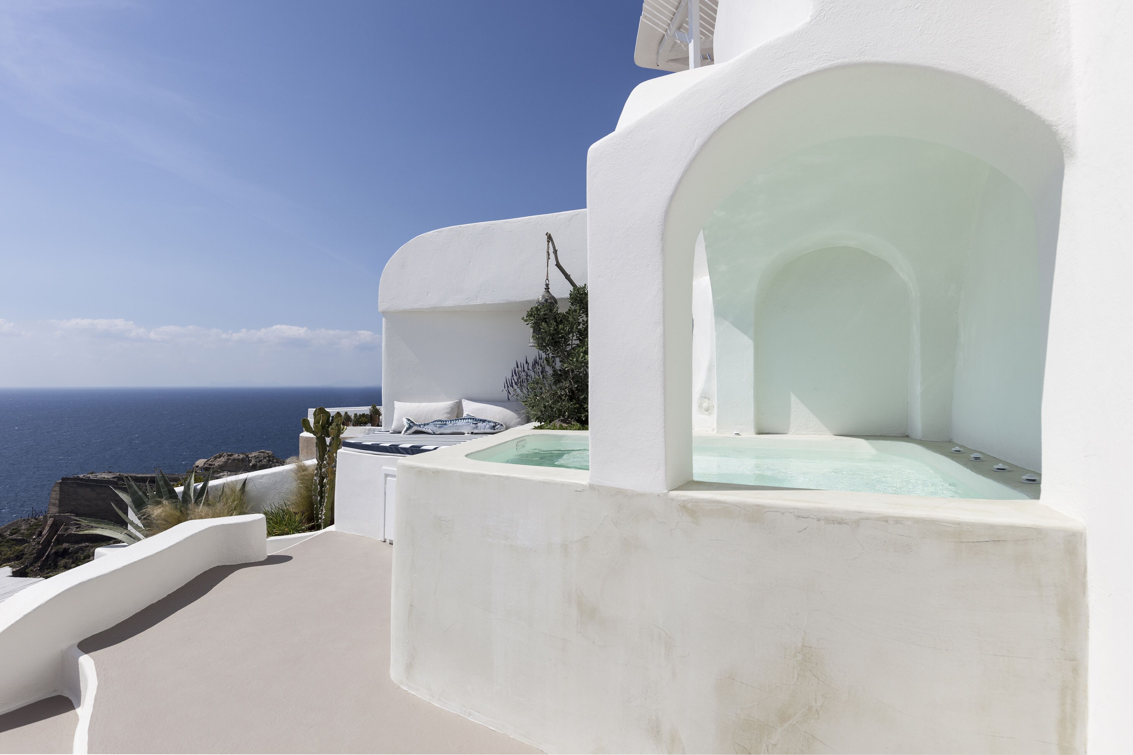 A white building with a hot tub and a view of the sea.