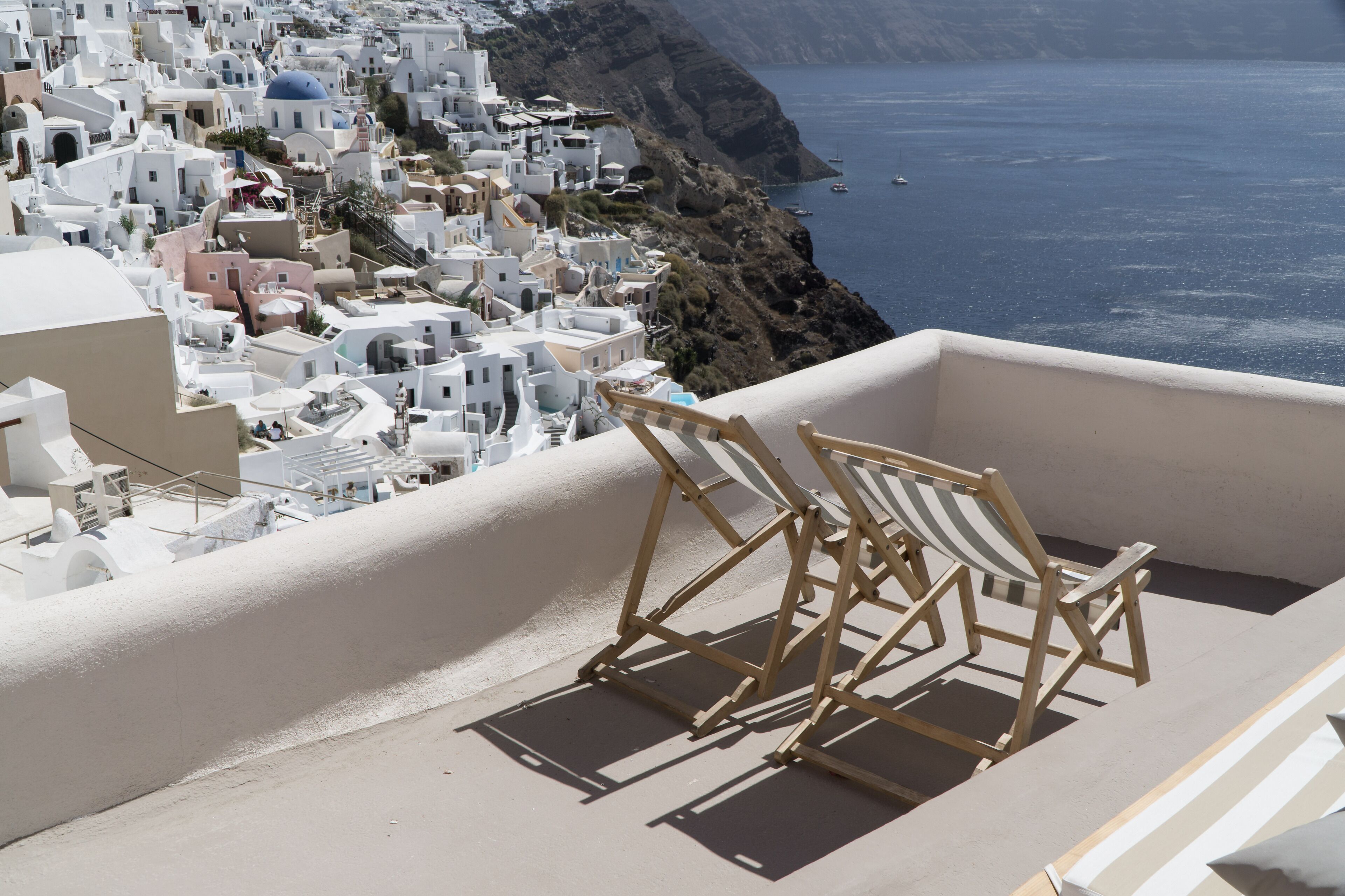 Un balcone con vista su una cittadina costiera, caratterizzata da edifici bianchi e un mare blu cristallino.