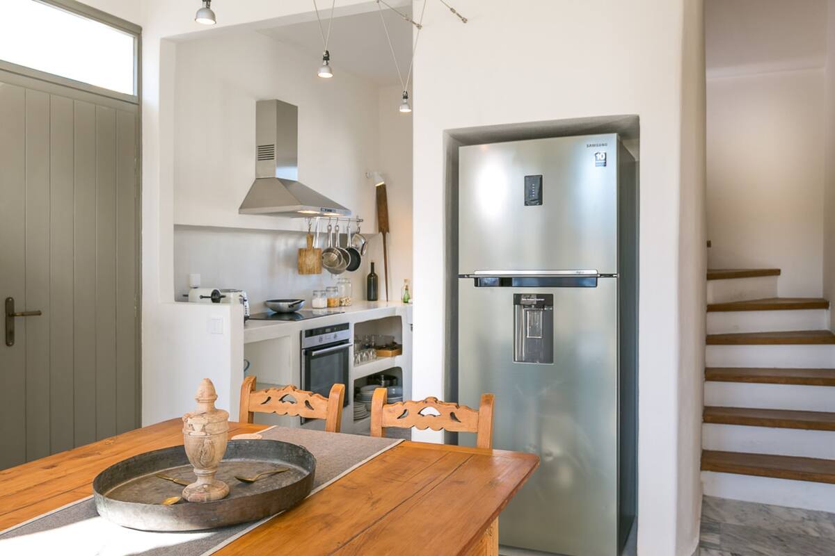 A modern kitchen with a stainless steel refrigerator, wooden dining table, and chairs.