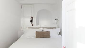 A white room with a bed, a door, and a wall-mounted lamp.