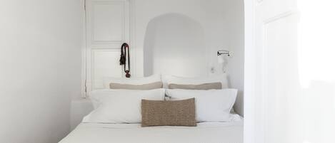 A white room with a bed, a door, and a wall-mounted lamp.
