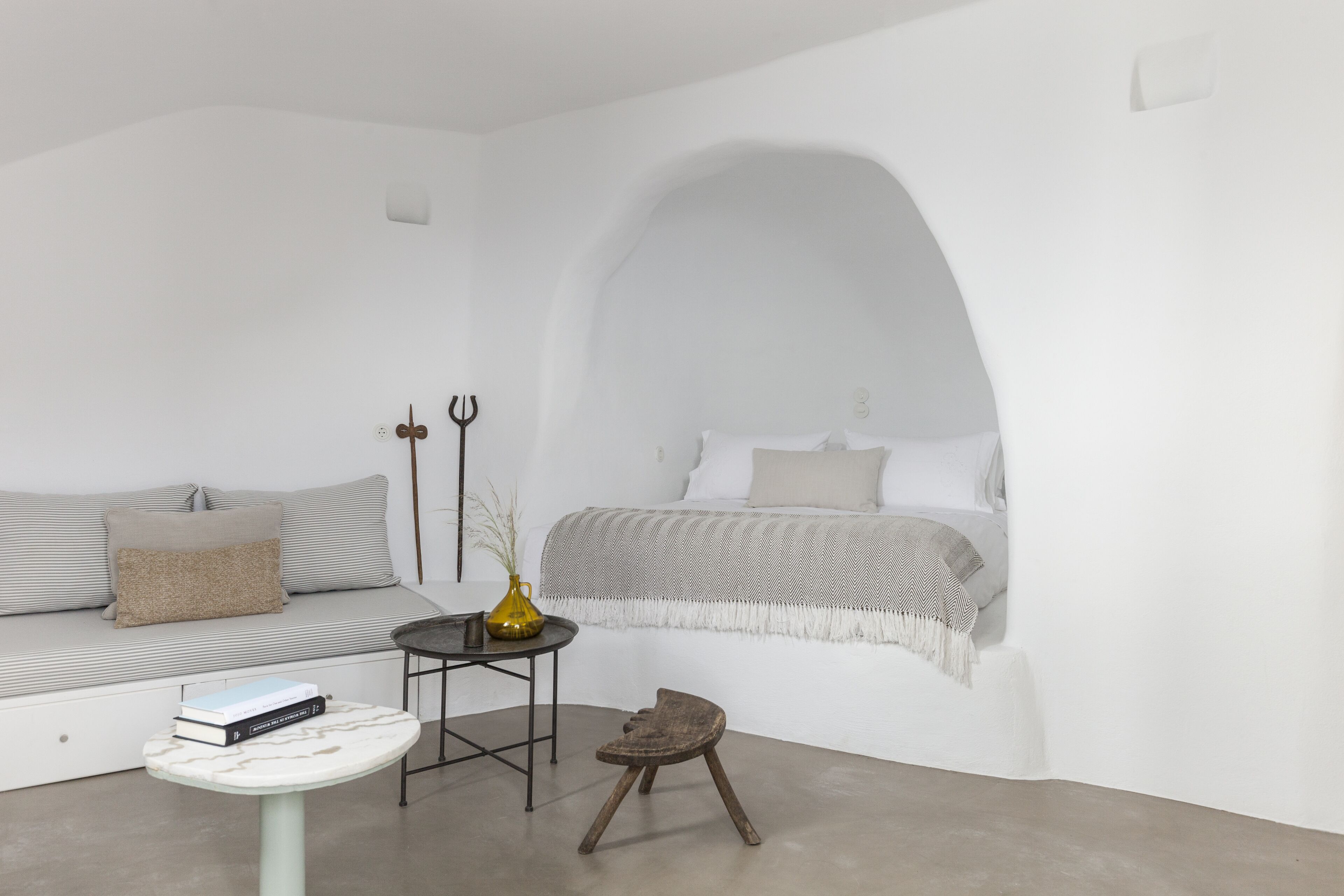 Une pièce au décor minimaliste, avec un canapé, une petite table, un vase décoratif et un lit recouvert d’une couverture à motifs.