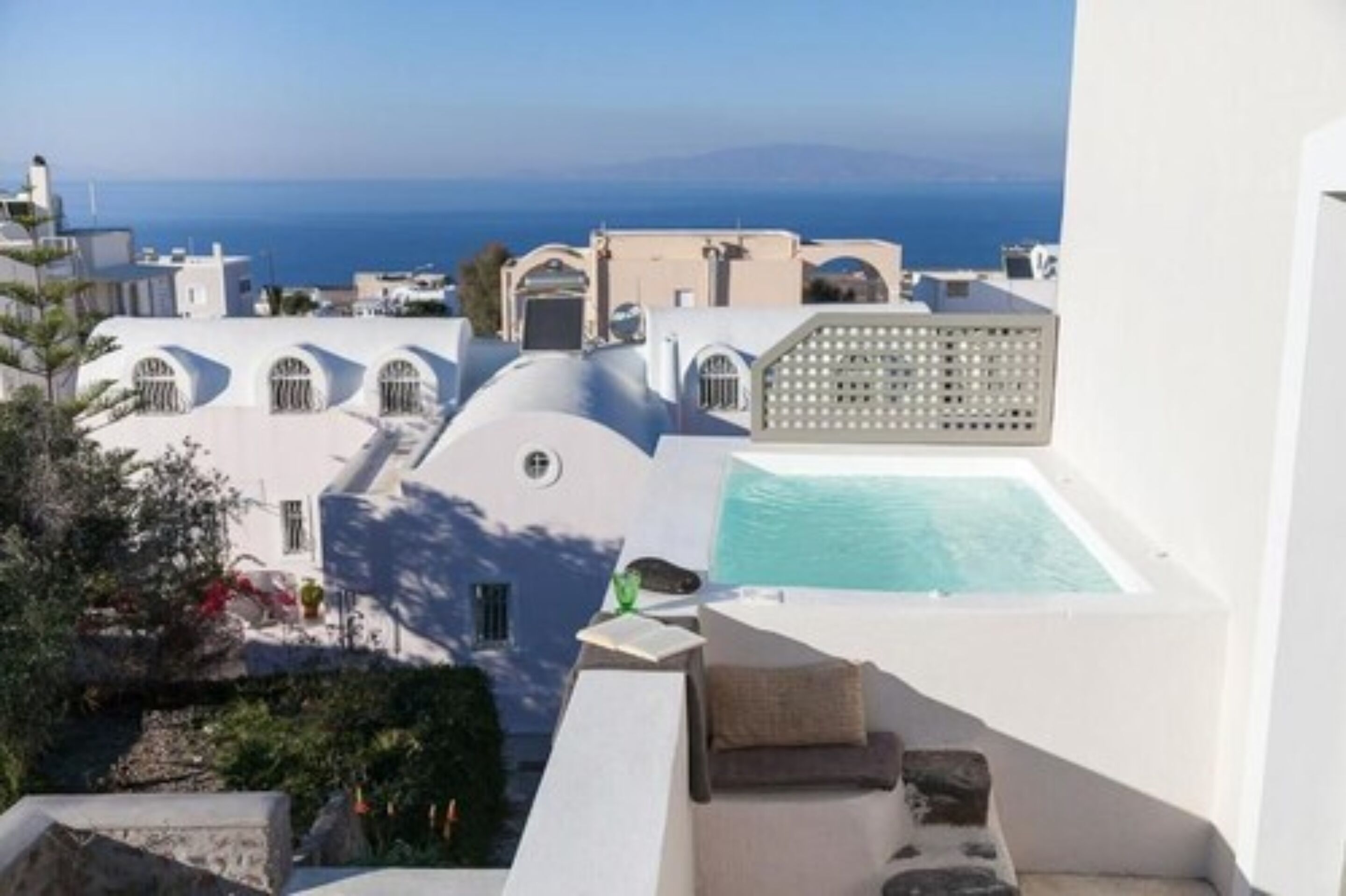 A rooftop with a swimming pool, white architecture, and a view of the sea.