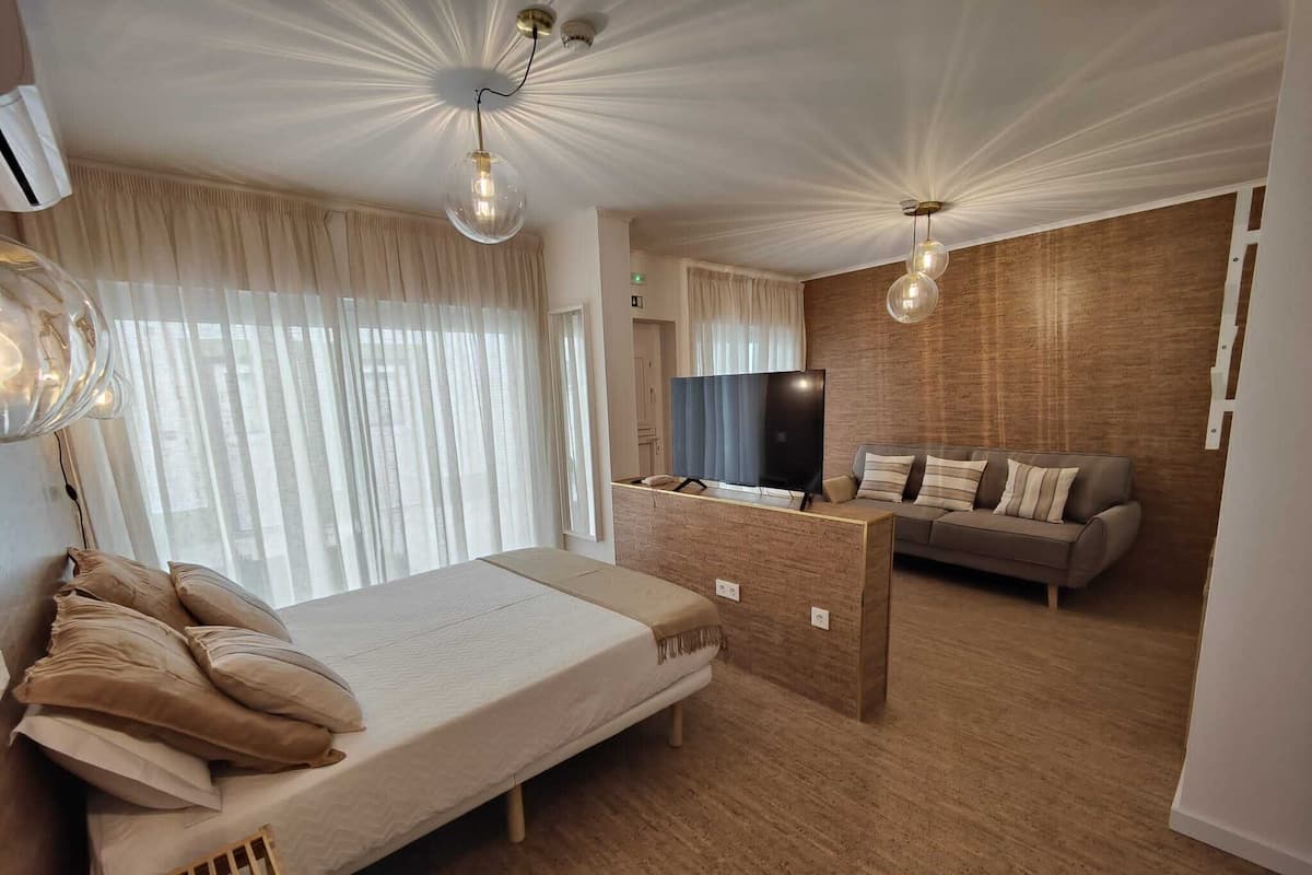 A modern hotel room with a large bed, a wooden desk, a television, and a sofa.